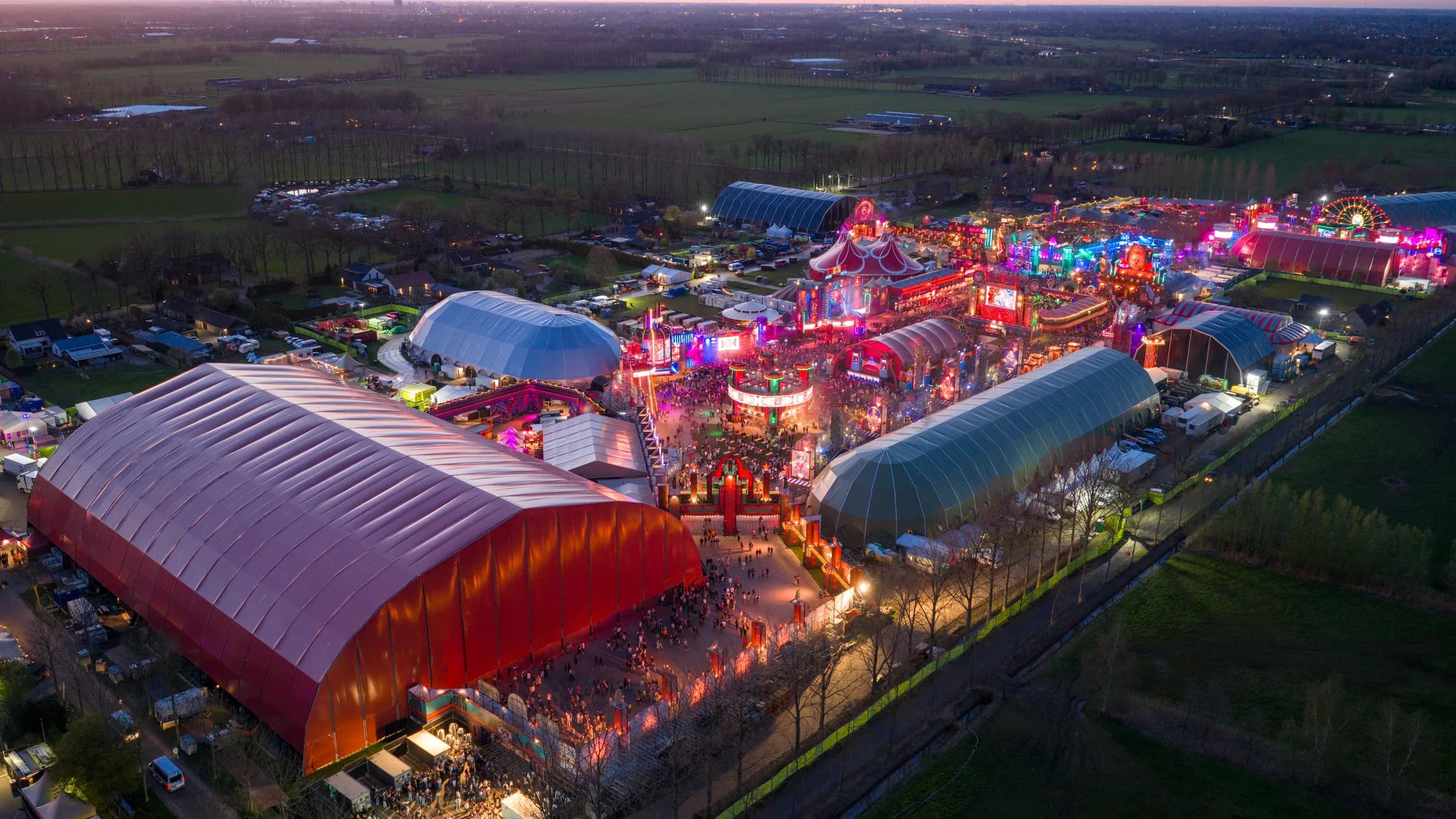 Luchtfoto van het festivalterrein van Paaspop in de schemering, met de overkapte podia, de kermis en het omliggende open landschap